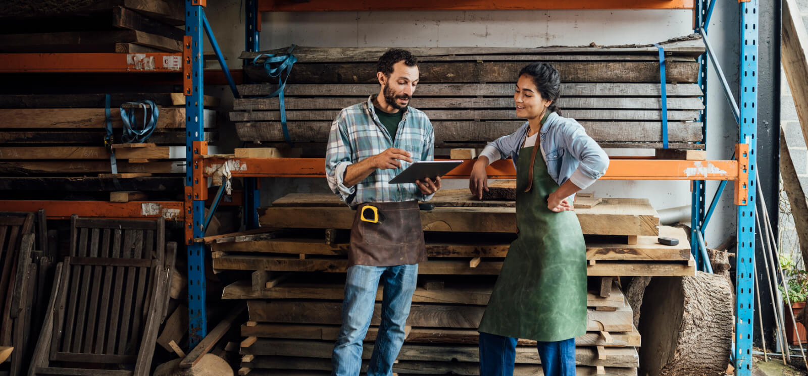 two workers in aprons with lumber stacked behind them