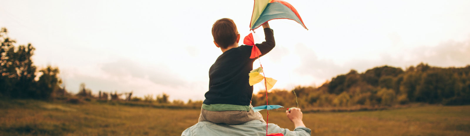 dad holding a kid with a kite on his shoulders